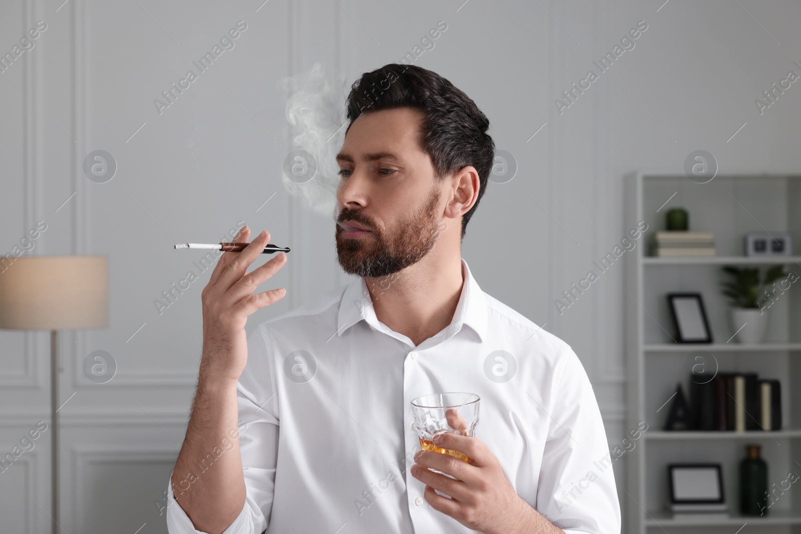 Photo of Man using cigarette holder for smoking and holding glass of whiskey in office