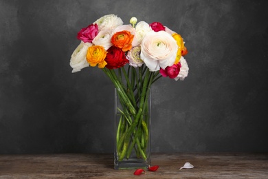 Photo of Vase with beautiful ranunculus flowers on wooden table against dark background
