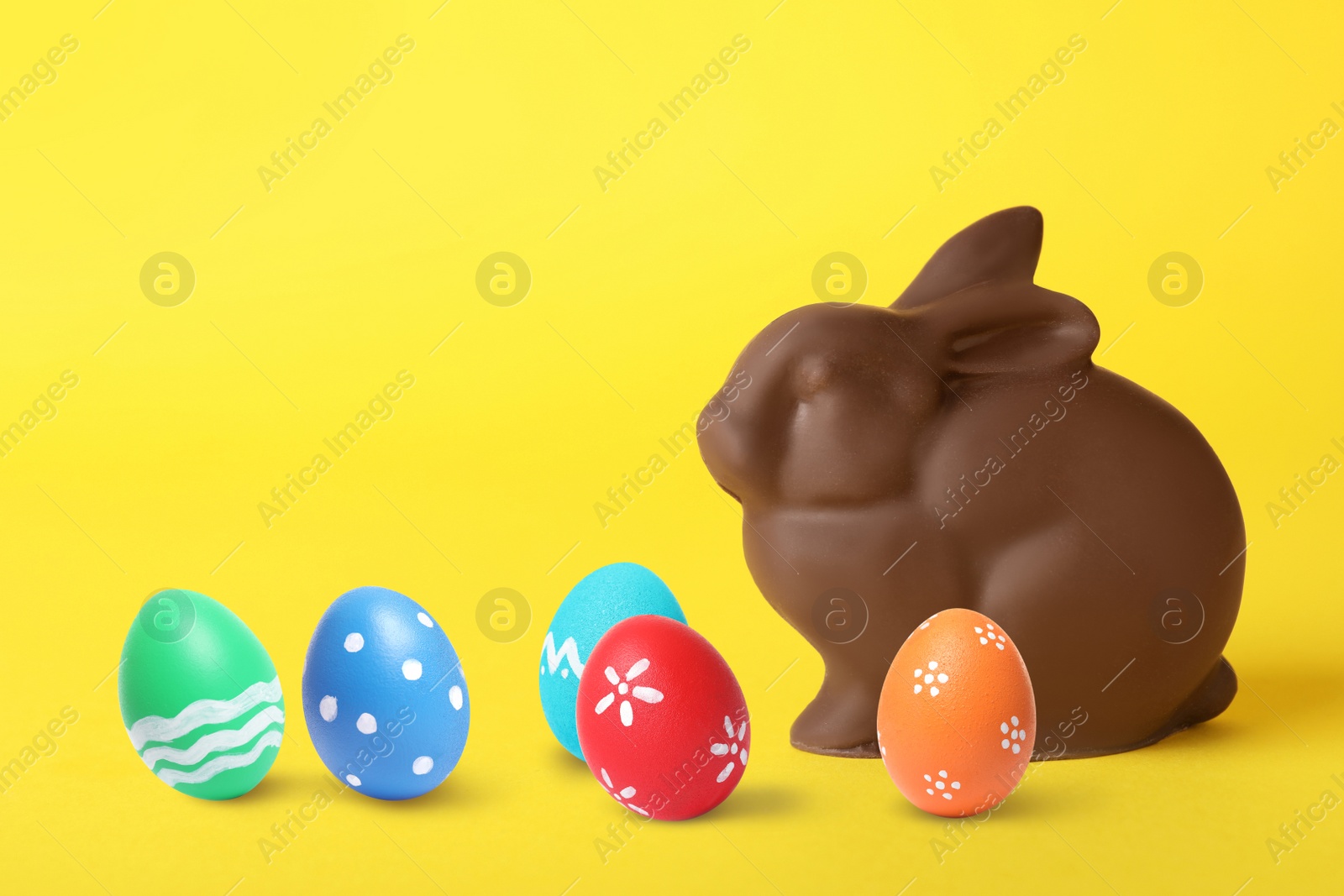 Image of Chocolate bunny and painted Easter eggs on yellow background