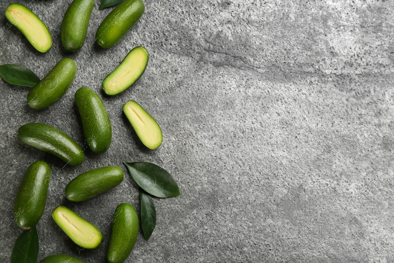 Photo of Fresh seedless avocados with green leaves on grey table, flat lay. Space for text