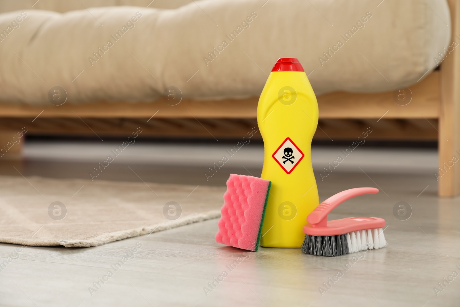 Photo of Bottle of toxic household chemical with warning sign, brush and scouring sponge in room, space for text