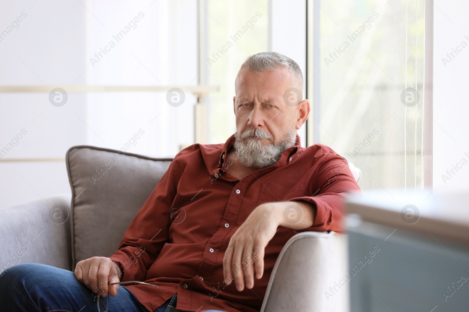 Photo of Depressed senior man sitting in armchair indoors