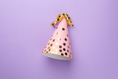 One pink party hat with serpentine streamers on purple background, top view