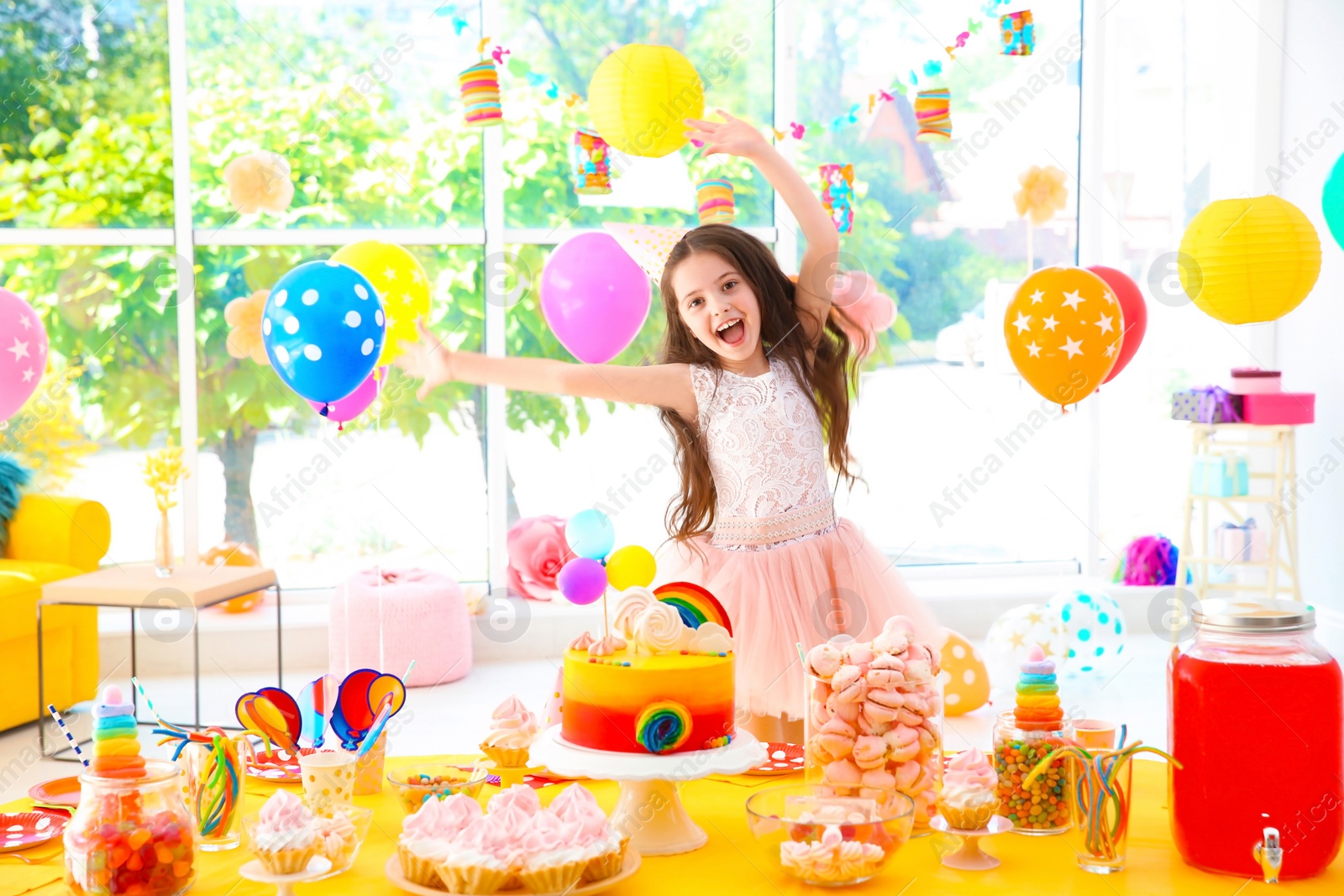 Photo of Cute little girl near table with treats at birthday party indoors