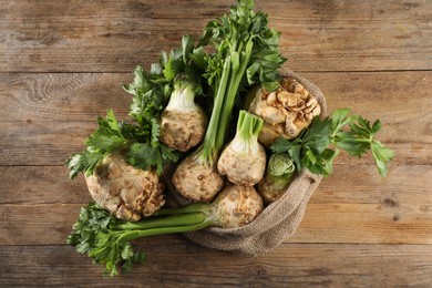 Fresh raw celery roots and sack on wooden table, top view
