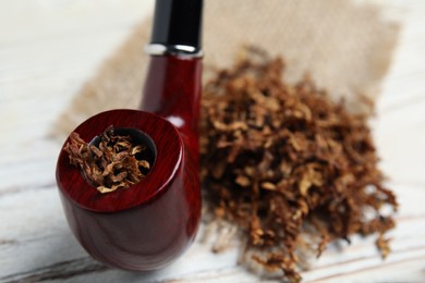Smoking pipe and dry tobacco on white wooden table, closeup
