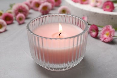 Stylish tender composition with burning candle and flowers on grey table. Cozy interior element