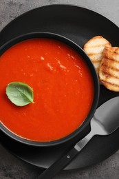 Delicious tomato cream soup in bowl and pieces of grilled bread served on dark textured table, top view