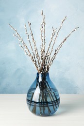 Photo of Beautiful pussy willow branches in vase on white wooden table against light blue background