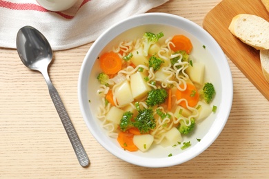 Bowl of fresh homemade vegetable soup served on wooden table, flat lay