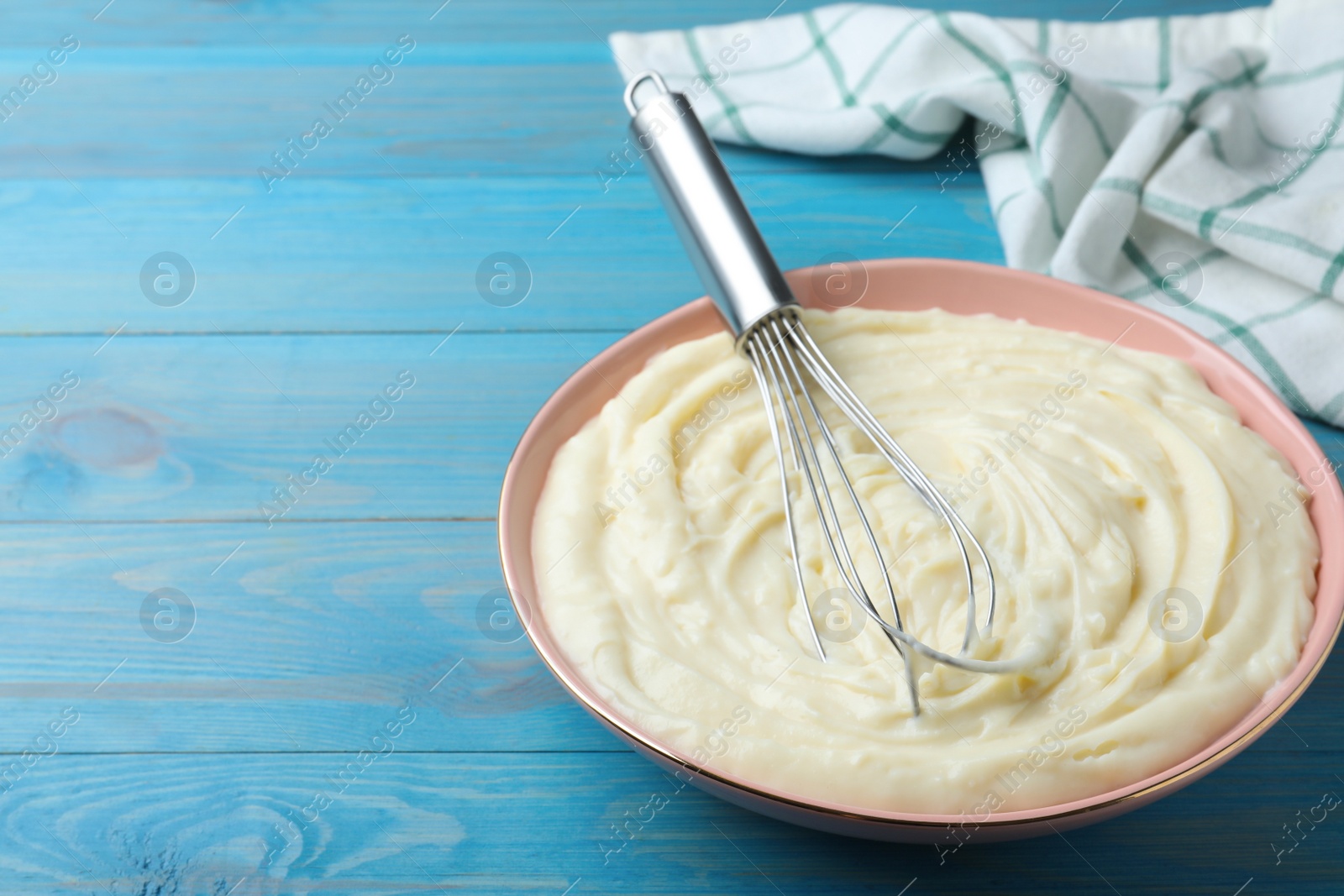 Photo of Pastry cream with balloon whisk on light blue wooden table. Space for text