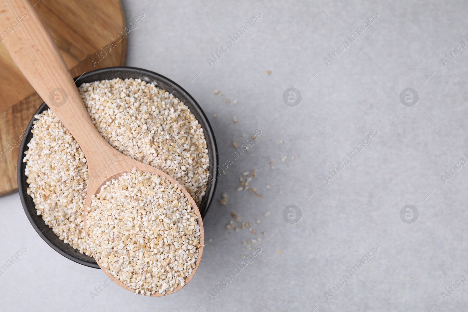 Photo of Dry barley groats in bowl and spoon on light grey table, top view. Space for text