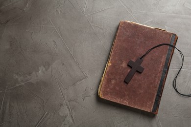 Photo of Wooden Christian cross and old Bible on grey table, top view. Space for text