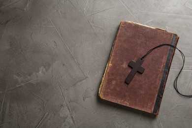 Wooden Christian cross and old Bible on grey table, top view. Space for text