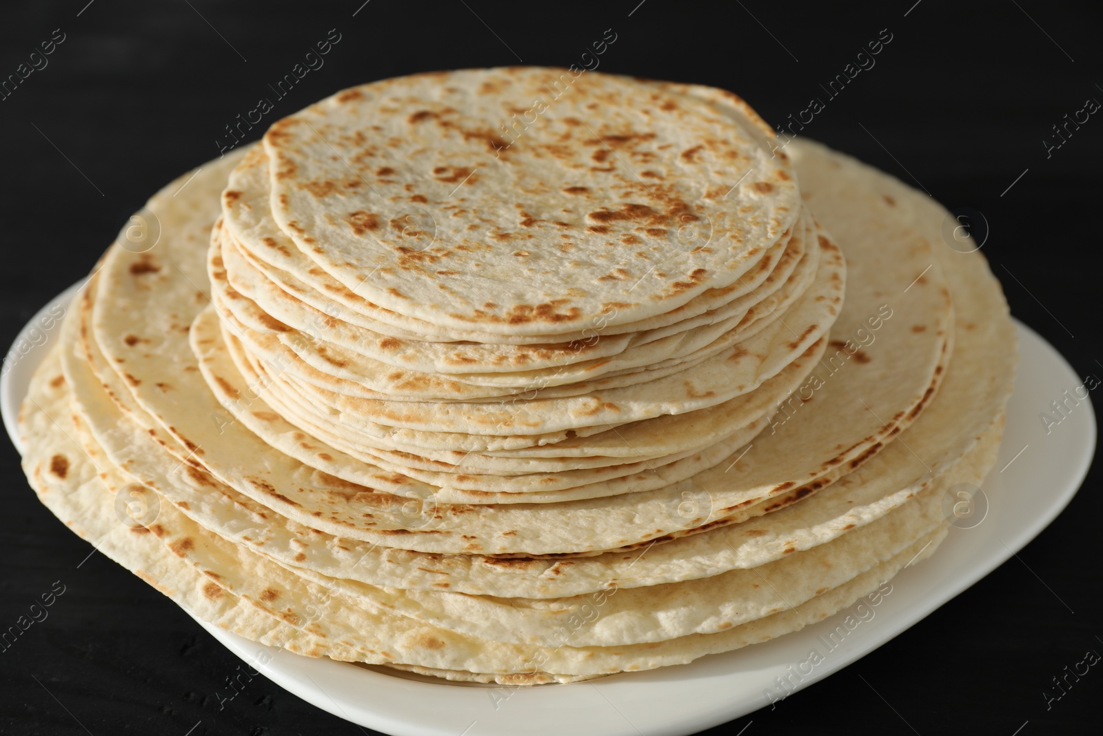 Photo of Many tasty homemade tortillas on black wooden table, closeup