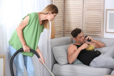 Lazy husband lying on sofa and his wife cleaning at home