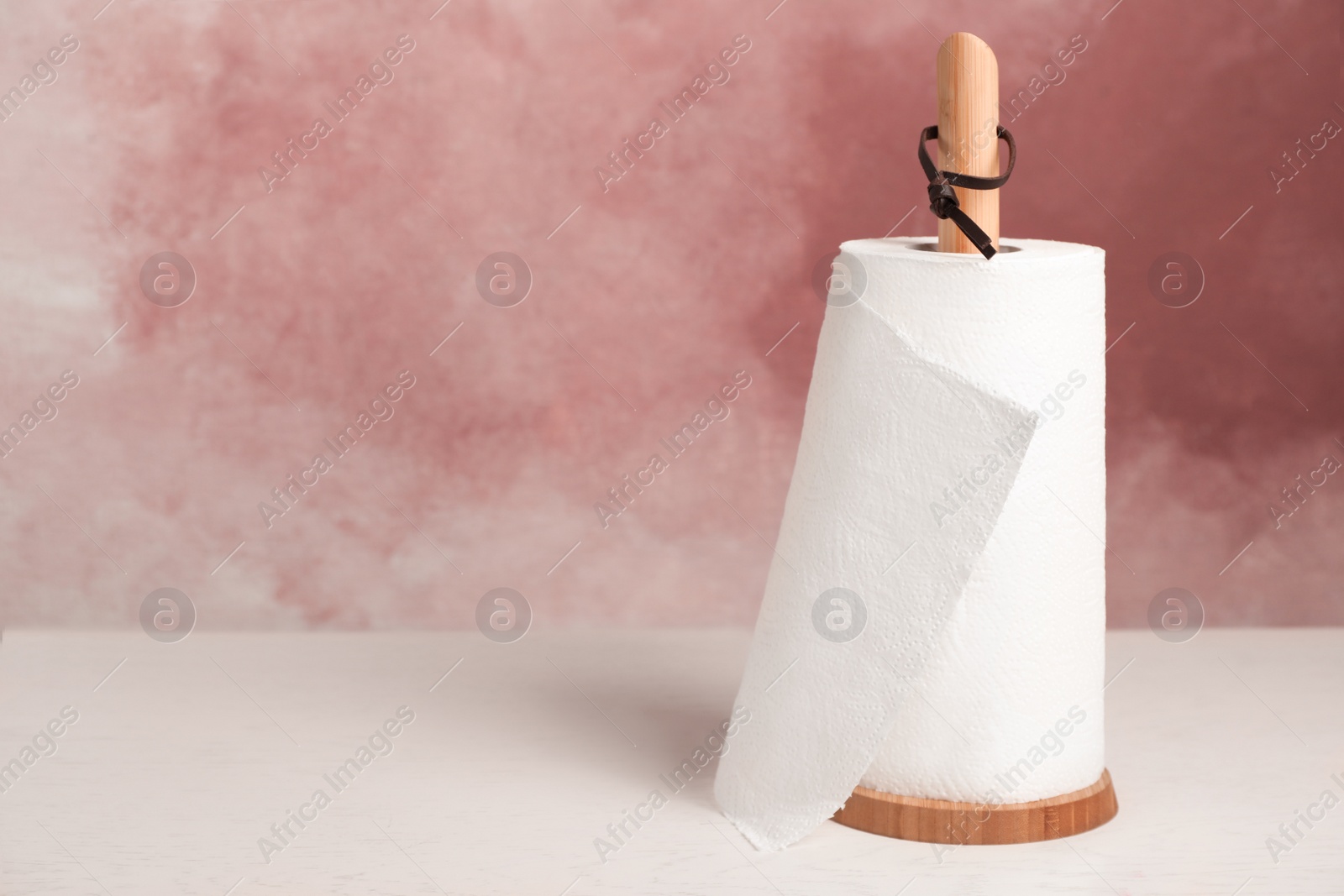 Photo of Holder with roll of paper towels on white wooden table near pink wall. Space for text