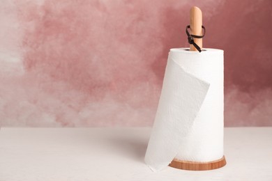 Holder with roll of paper towels on white wooden table near pink wall. Space for text