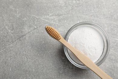 Bamboo toothbrush and bowl of baking soda on grey table, top view. Space for text