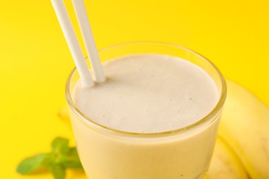 Photo of Glass of tasty banana smoothie with straws on yellow background, closeup