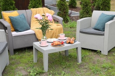 Photo of Breakfast served outdoors. Morning drink, food and vase with flowers on rattan table