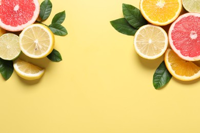 Different cut citrus fruits and leaves on yellow table, flat lay. Space for text