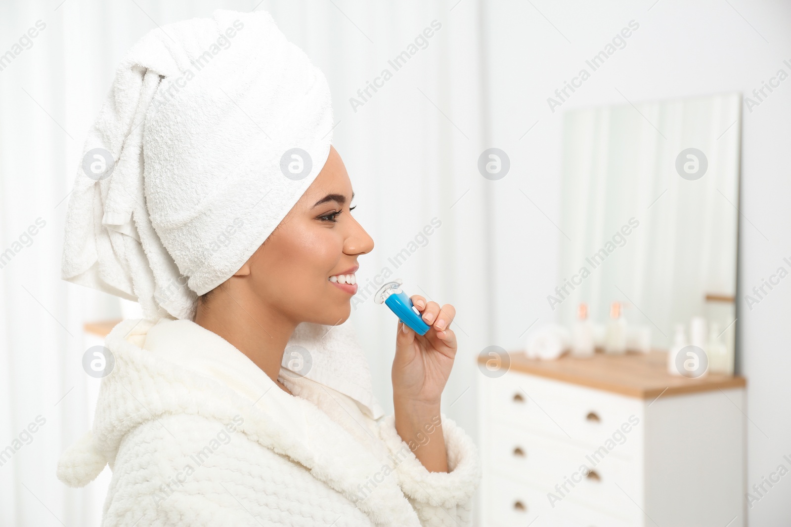 Photo of Young African-American woman using teeth whitening device at home