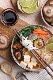 Photo of Vegetarian ramen, chopsticks and ingredients on light textured table, flat lay