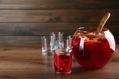 Photo of Bowl of delicious aromatic punch drink and glasses on wooden table. Space for text