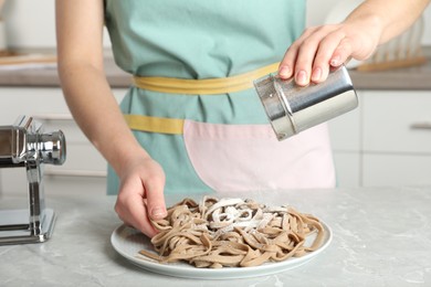 Photo of Woman sprinkling raw soba (buckwheat noodles) with flour at grey table in kitchen, closeup