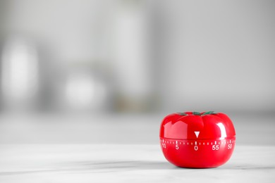 Photo of Kitchen timer in shape of tomato on white marble table against blurred background. Space for text