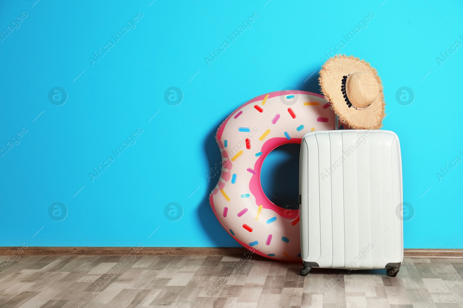 Photo of Suitcase with hat and inflatable ring on floor near color wall. Space for design
