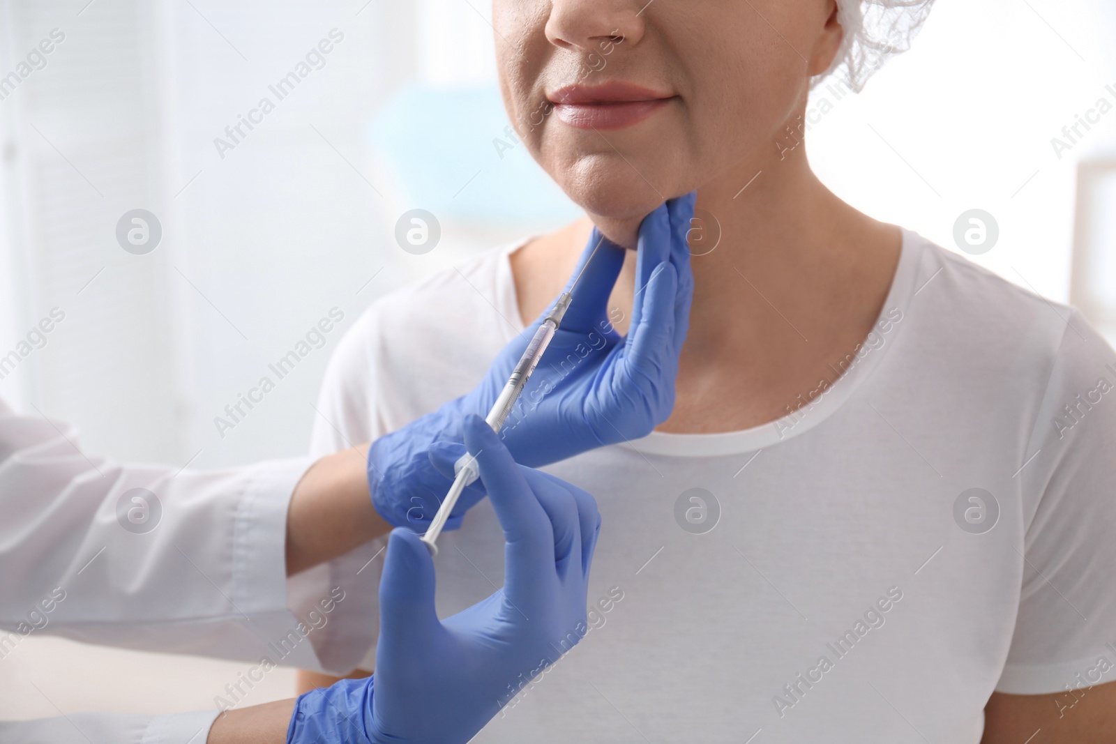 Photo of Mature woman with double chin receiving injection in clinic, closeup