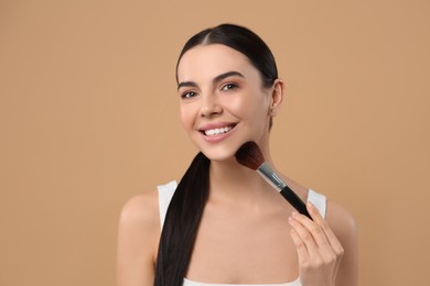 Beautiful woman applying makeup on light brown background