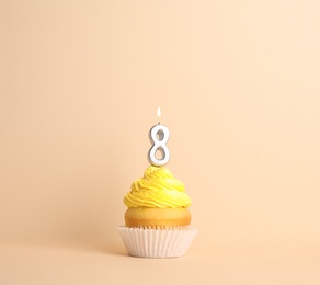 Photo of Birthday cupcake with number eight candle on beige background