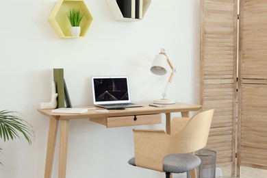 Cozy workspace with modern laptop on desk and comfortable chair at home