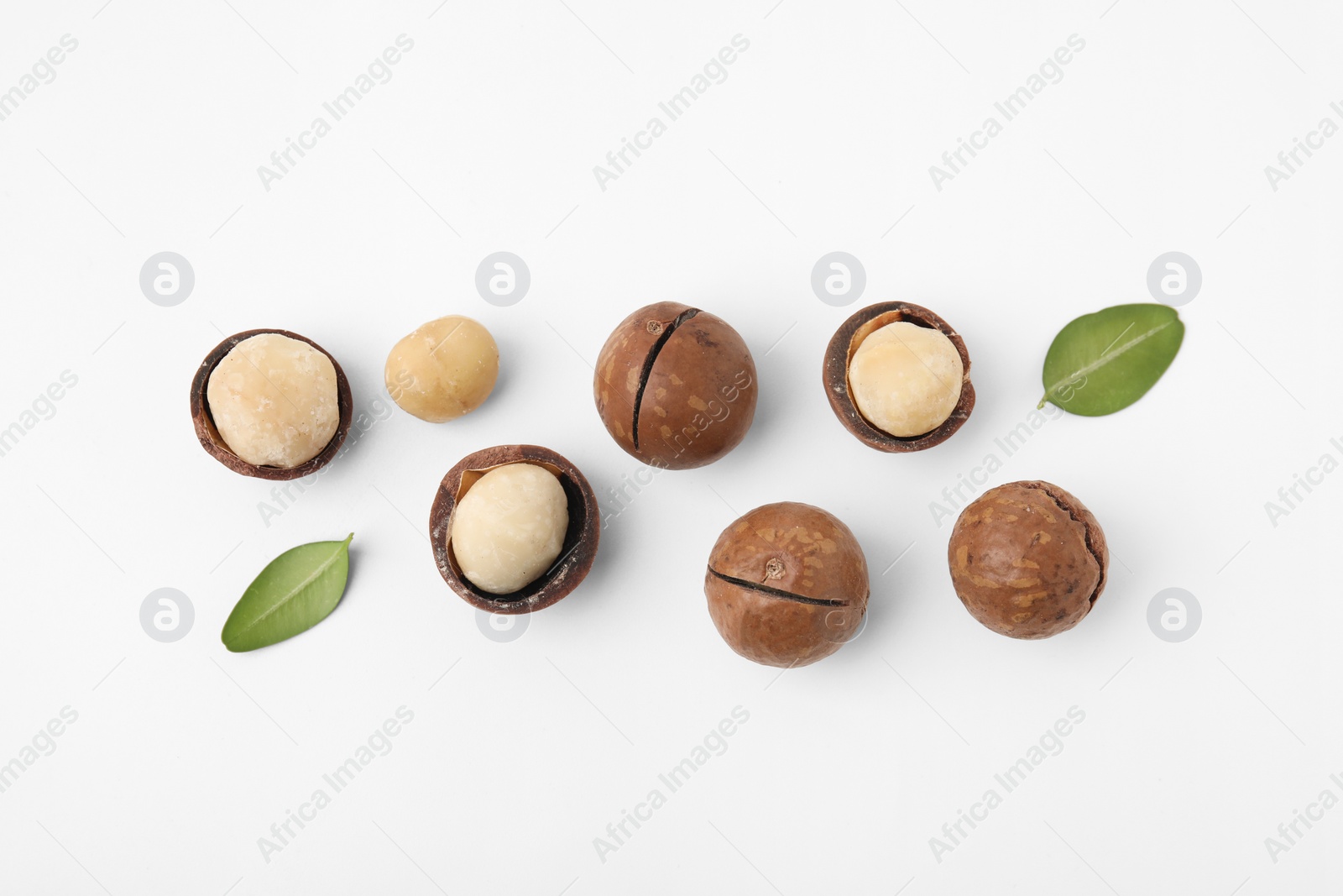 Photo of Tasty Macadamia nuts and green leaves on white background, flat lay