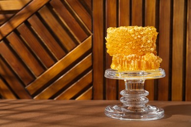 Glass stand with natural honeycombs on wooden table, space for text