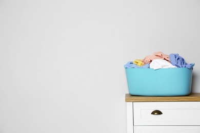 Photo of Plastic laundry basket with dirty clothes on chest of drawers near light wall. Space for text