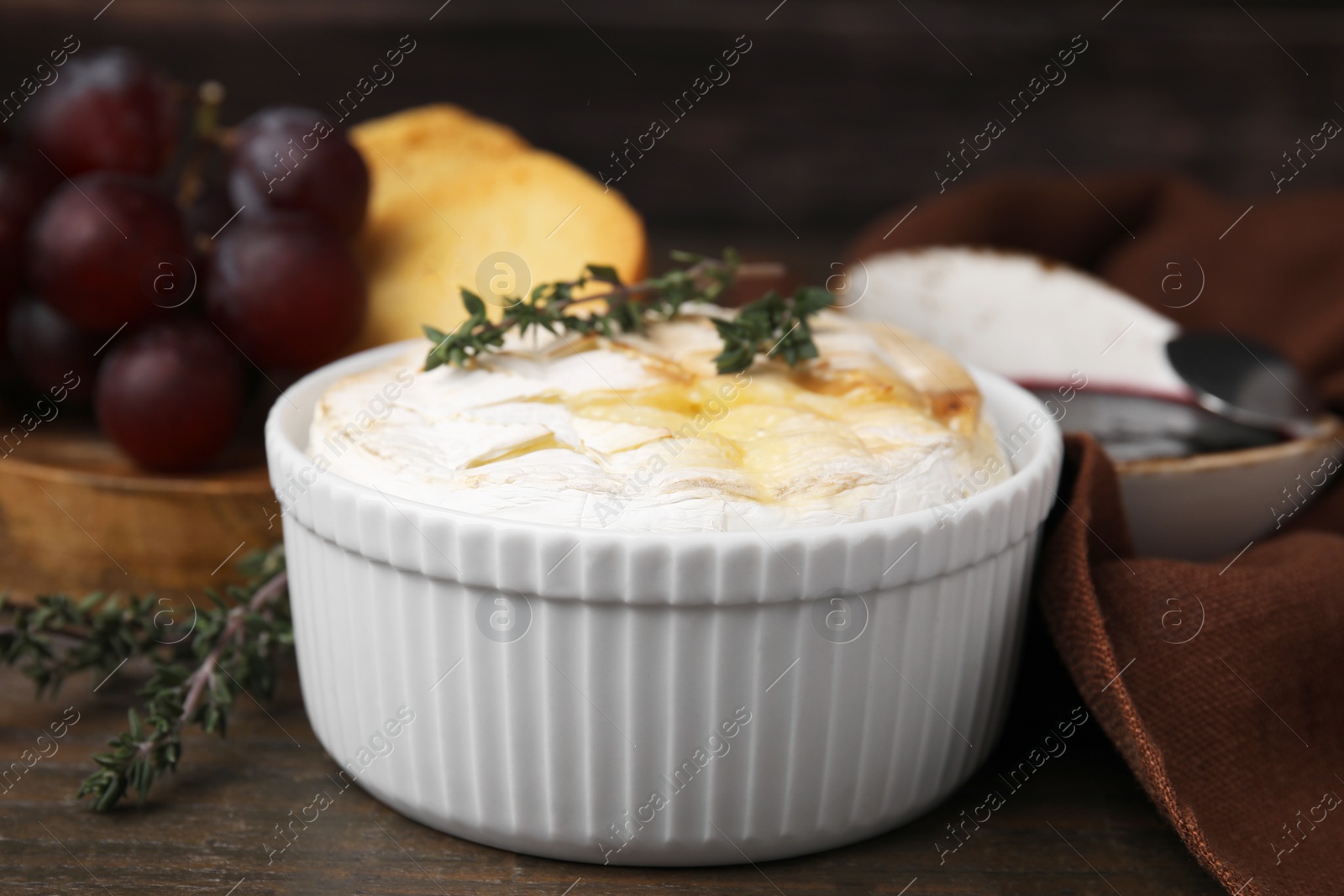 Photo of Tasty baked camembert and thyme in bowl on wooden table, closeup