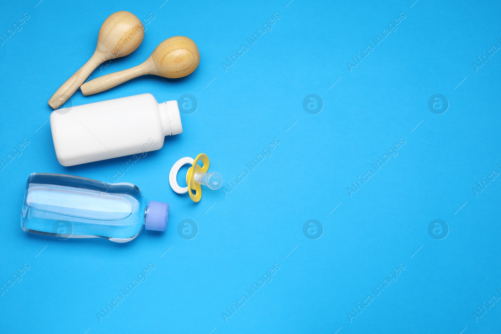 Photo of Wooden maracas, pacifier and baby care products on light blue background, flat lay. Space for text