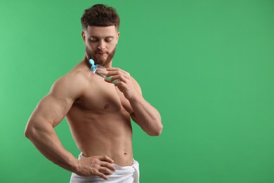 Handsome man applying lotion onto his shoulder on green background, space for text