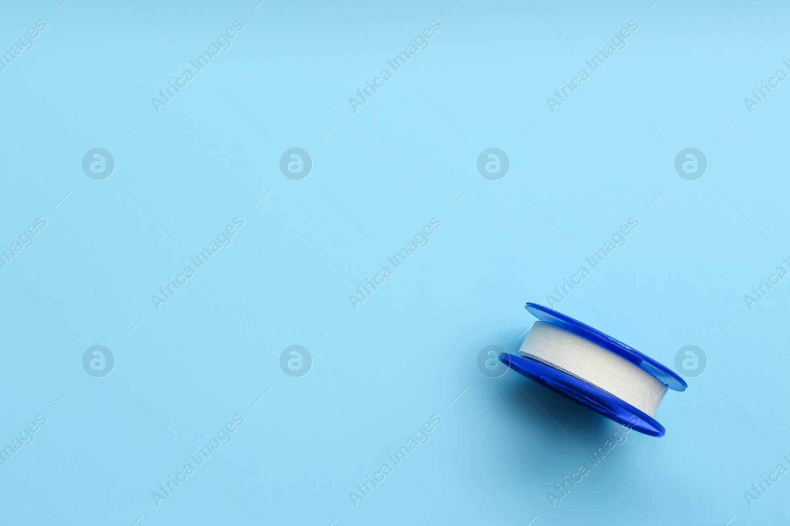 Photo of Sticking plaster roll on light blue background, top view. Space for text