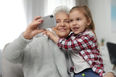Photo of Cute girl and her grandmother taking selfie  at home