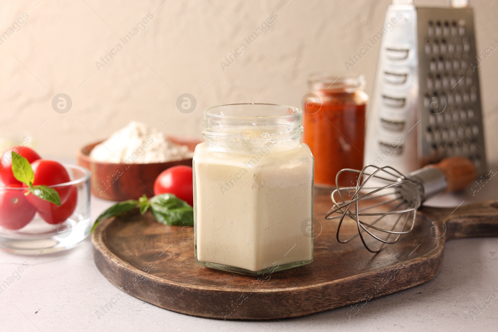 Photo of Pizza dough starter in glass jar, products and whisk on gray table