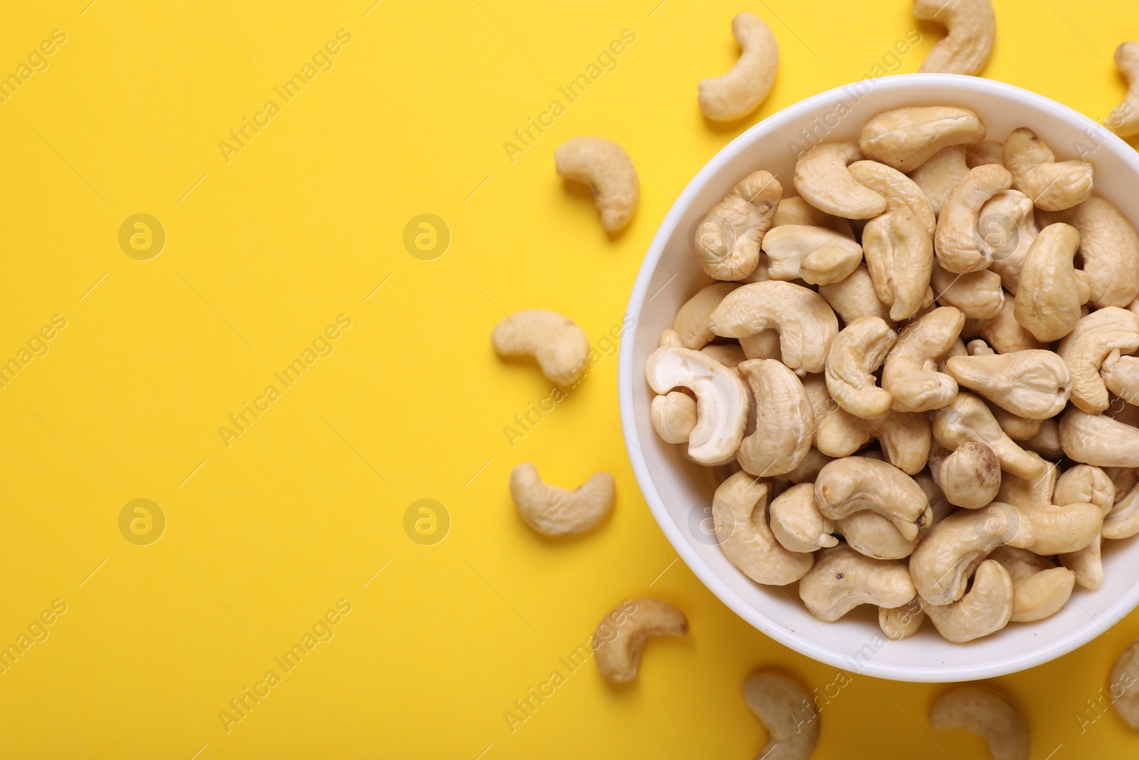 Photo of Tasty cashew nuts on yellow background, top view. Space for text