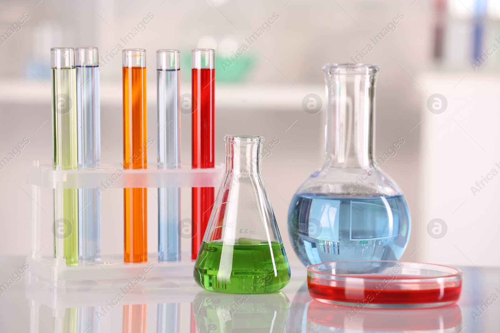 Photo of Laboratory analysis. Glass flasks, Petri dish and test tubes with liquids on white table against blurred background