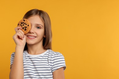 Photo of Cute girl with chocolate chip cookie on orange background. Space for text