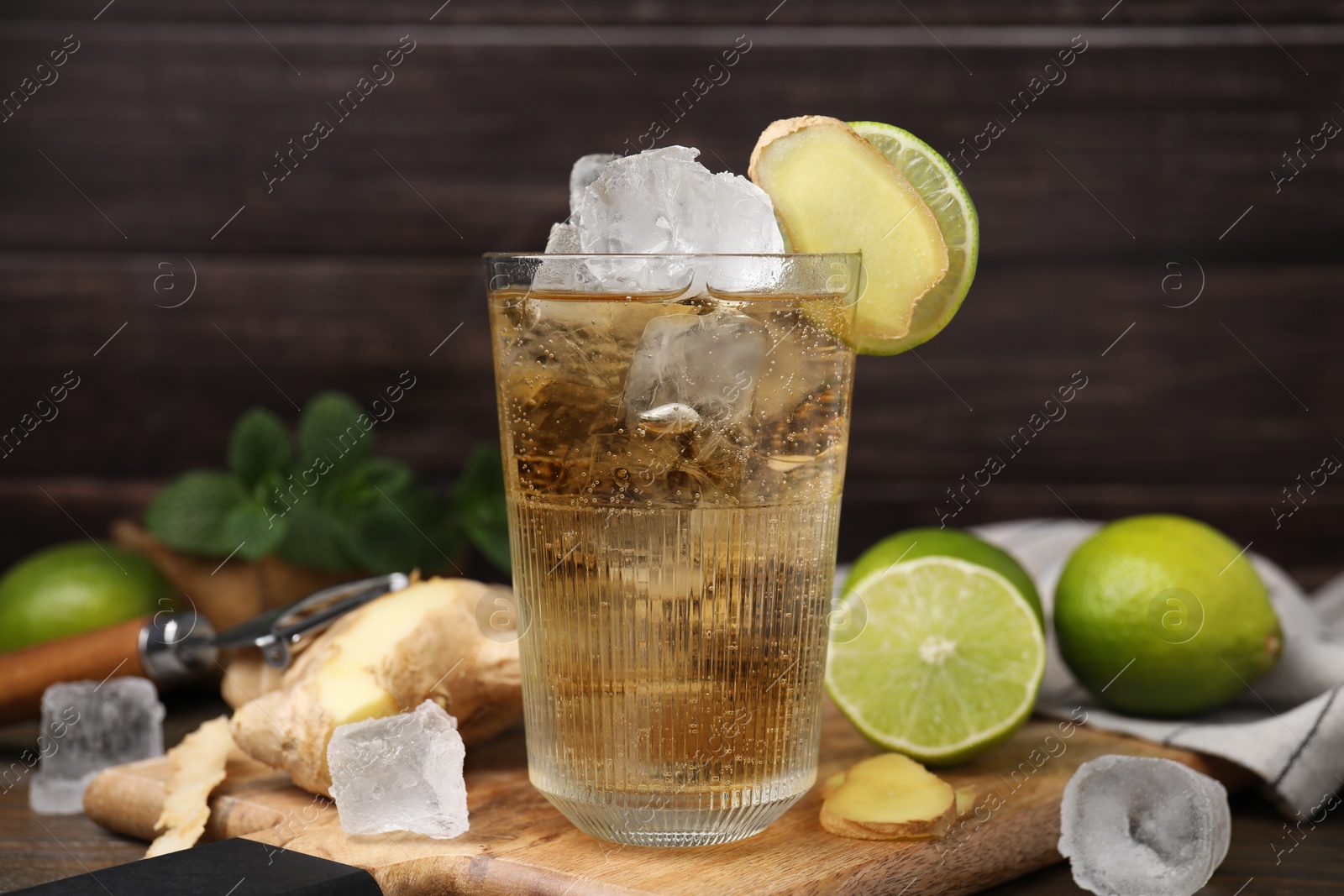 Photo of Glass of tasty ginger ale with ice cubes and ingredients on wooden table