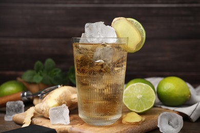 Glass of tasty ginger ale with ice cubes and ingredients on wooden table